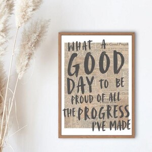 May include: A framed print with a beige background and black text that reads "What a good day to be proud of all the progress I've made".