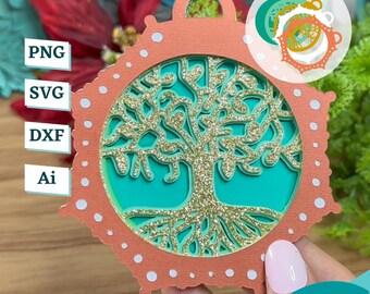 May include: A coral-colored Christmas ornament with a white dotted border. The ornament features a gold glitter tree of life design with teal green leaves and roots.