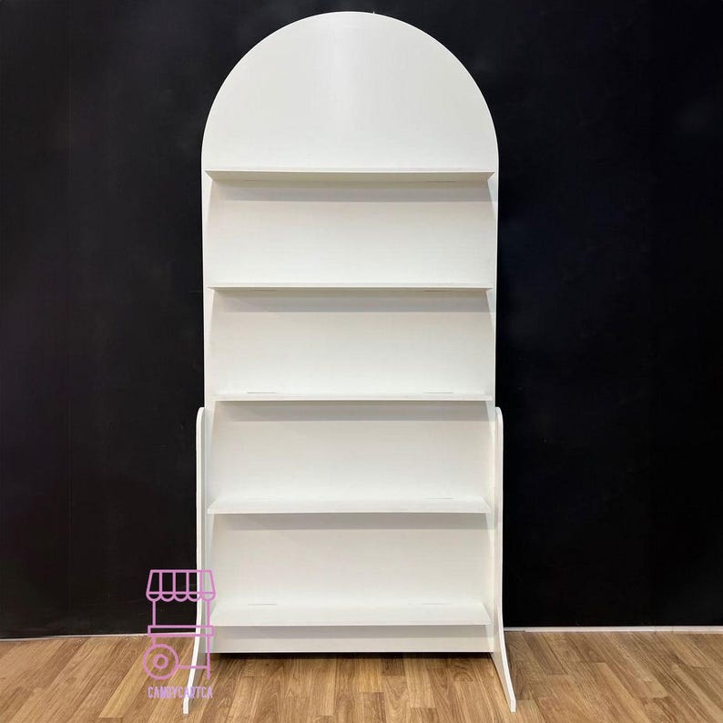 Puede incluir: Una estanter&iacute;a de exhibici&oacute;n blanca en forma de arco con cuatro estantes horizontales. La estanter&iacute;a tiene una parte superior redondeada y una base robusta. El fondo es de color oscuro y la estanter&iacute;a est&aacute; colocada sobre un suelo de madera. El dise&ntilde;o es sencillo y moderno.