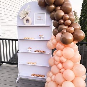 A beautifully designed arched party backdrop featuring built-in shelves, perfect for showcasing decorations, party favors, or other items at events and gatherings. Ideal for creating a stylish and functional display at any celebration.