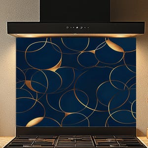 May include: A navy blue kitchen backsplash with a gold circular pattern. The design features overlapping gold lines and filled-in gold circles. The backsplash is installed above a black gas stove and below a black range hood.