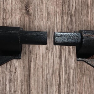 Könnte beinhalten: Zwei schwarze, 3D-gedruckte Kunststoffteile, eines mit einer langen, geraden, zylindrischen Verlängerung und das andere mit einer kürzeren, gebogenen Verlängerung. Beide Teile haben eine flache, abgewinkelte Basis.
