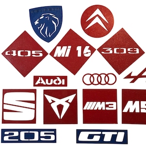 Op de afbeelding: Een verzameling autologo's en -emblemen, waaronder Audi, Peugeot, Citroën en BMW. De logo's zijn uit rood en blauw vinyl geknipt en zijn in een willekeurig patroon op een witte achtergrond gerangschikt.