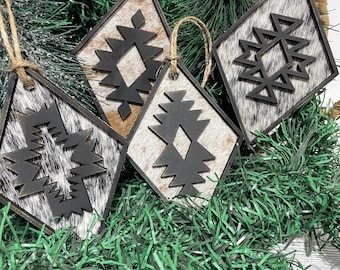 May include: Four diamond-shaped Christmas ornaments with a black geometric design and a cowhide pattern. Each ornament has a black border and a jute string for hanging. The ornaments are displayed on green garland and near a pinecone.