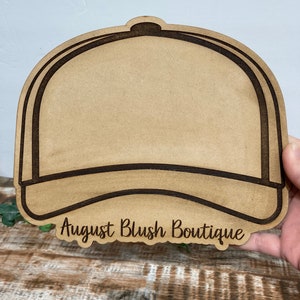 May include: A brown wooden cutout of a baseball cap with the text "August Blush Boutique" at the bottom.