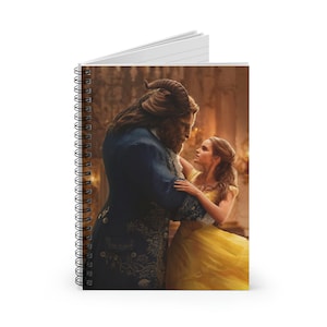 May include: A spiral bound notebook featuring a scene from the movie Beauty and the Beast. The Beast, a blue-furred humanoid creature, is holding Belle, a woman in a yellow dress, in his arms. They are looking at each other with love and affection.