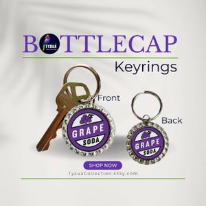 May include: Grape Soda bottle cap keychain with a purple grape design and the words "Grape Soda" on a white background. The keychain is attached to a silver key ring.
