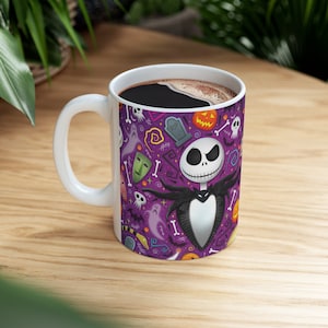 May include: White ceramic mug with a Halloween design featuring Jack Skellington, ghosts, pumpkins, and other spooky elements on a purple background. The mug has a white handle and is filled with dark coffee.