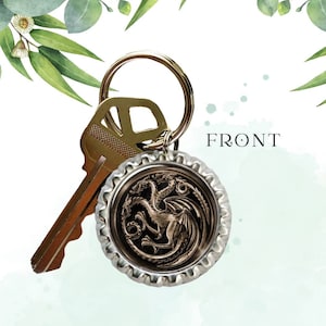 May include: A gold-colored key chain with a silver bottle cap charm featuring a three-headed dragon design. The text "FRONT" is visible on the image.