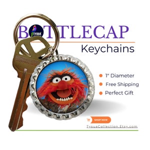 May include: A keychain featuring a 1-inch diameter bottle cap with a picture of the Muppet character Animal. The bottle cap is attached to a silver key ring.