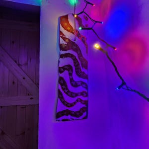 Könnte beinhalten: Ein rechteckiges, handbemaltes Holzschild mit patriotischem Thema, das rote und weiße Streifen und Sterne aufweist. Das Schild hängt an einer weißen Wand und wird von bunten Lichterketten beleuchtet. Das Schild ist etwa 30 cm lang.