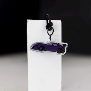 May include: A purple car keyring with a black metal clip. The car is a sports car with a spoiler and black wheels.