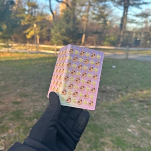 May include: A pink and yellow wallet with a repeating pattern of brown money bags and gold stars.