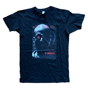 May include: Black t-shirt with a white and gray print of the movie poster for 12 Monkeys. The poster features Bruce Willis, Madeleine Stowe, and Brad Pitt. The text on the poster reads "The future is different! 12 Monkeys".