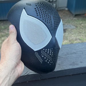 May include: A black textured mask featuring two large, white, mesh-covered eye openings. The surface of the mask is covered in a pattern of small, circular perforations across the forehead and nose area, creating a distinct, ventilated appearance.
