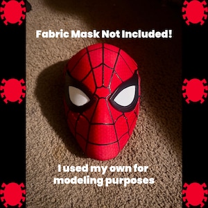 Op de afbeelding: Een rood en zwart Spider-Man gezichtsmasker met witte ooglenzen, voorzien van een gestructureerd webpatroon. De tekst Fabric Mask Not Included! en I used my own for modeling purposes staat op de afbeelding met rode spinneniconen.