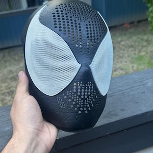 May include: A black full-face mask featuring large, white, mesh-covered eye openings. The black surface of the mask has a textured, dotted pattern across the forehead and cheek areas, creating a distinct contrast with the smooth white eye lenses.