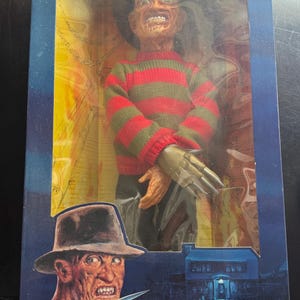 Może przedstawiać: Figurka akcji Talking Freddy Krueger firmy Matchbox z serii A Nightmare on Elm Street w oryginalnym opakowaniu. Pudełko zawiera tekst Hi, I'm Freddy! See back panel, Talking Freddy Krueger oraz My arms and legs are poseable.