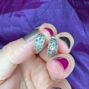 Puede incluir: Un par de pendientes de aro de plata con engaste pavé de pequeñas piedras transparentes.