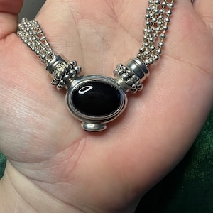 May include: A silver necklace with multiple strands of small beads and a black oval pendant.