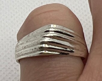 May include: A silver ring with a textured, ridged design. The ring is worn on a finger.