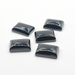 Peut inclure: Cinq pierres précieuses rectangulaires noires avec une finition brillante. Les pierres précieuses sont disposées sur une surface blanche.