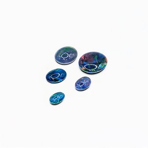 May include: Five oval-shaped black opal cabochons of varying sizes. The opals have a dark blue, green, and red iridescent sheen.