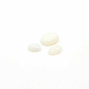 May include: Three white oval-shaped opal gemstones of varying sizes.