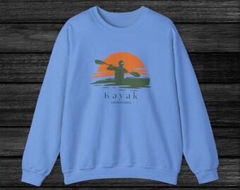 Puede incluir: Una sudadera de color azul claro con un gráfico de una persona haciendo kayak frente a un sol poniente. El texto "Kayak Adventures" está impreso debajo del gráfico.