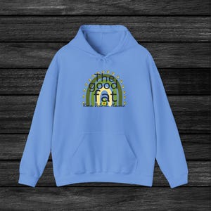 May include: A light blue hoodie with a graphic of a rainbow made of avocados. The text "The good fat" is in the center of the rainbow, and "Kona District, Hawaii" is below the rainbow.