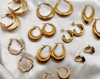 May include: A collection of gold hoop earrings in various styles and sizes. The earrings are arranged on a white satin fabric background.