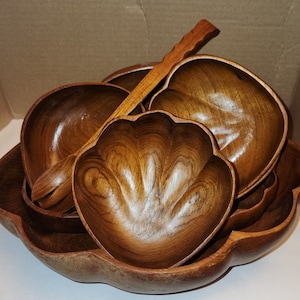 May include: A set of four wooden salad bowls with a wooden serving spoon. The bowls are nested inside each other and have a natural wood finish.