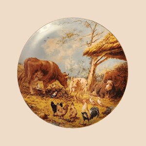 May include: A round ceramic plate with a colorful painting of a farmyard scene. The plate features a brown cow, a white pig, a brown and white cow, and several chickens. The background is a blue sky with white clouds and a thatched roof.