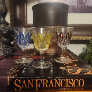 Puede incluir: Tres pequeños vasos de chupito de vidrio transparente con diseños de colores. Los vasos tienen un diseño azul, amarillo y rojo. Los vasos están sobre un libro con las palabras "San Francisco" impresas en la portada.