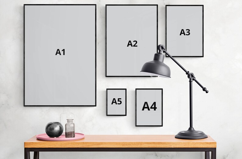 May include: Five black picture frames of different sizes hanging on a white wall. The frames are labeled A1, A2, A3, A4, and A5. A black lamp with a round shade is positioned in front of the frames.