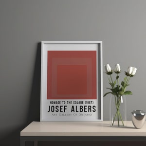 Op de afbeelding: Een ingelijste print van een rood abstract schilderij getiteld "Hommage aan het Vierkant (1967)" van Josef Albers. De print is van de Art Gallery of Ontario.