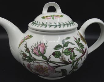 May include: White ceramic teapot with a lid and handle. The teapot is decorated with pink roses, green leaves, and a butterfly design. The teapot has a curved spout and a loop handle.
