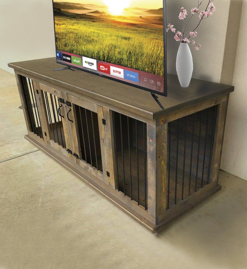 May include: A rustic wooden TV stand with two built-in dog kennels. The stand is stained a dark brown color and has black metal bars on the kennels. The stand has a flat top surface with a TV on top. The TV is displaying a screen with various streaming services.