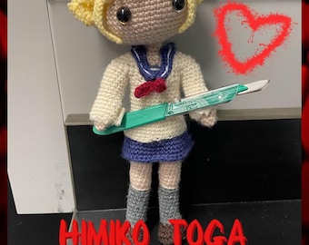 May include: Crocheted amigurumi doll of a girl with blonde hair, wearing a white sailor uniform and holding a scalpel. The doll is standing on a black and white tiled floor. The text "HIMIKO TOGA PDF PATTERN ONLY" is written in red letters at the bottom of the image.