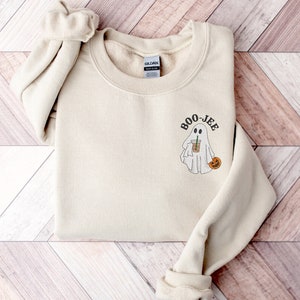 May include: A beige sweatshirt with a ghost holding a cup of coffee and a pumpkin. The text "BOO-JEE" is above the ghost.