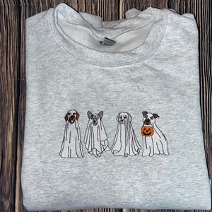 以下が含まれることがあります： ハロウィン用のゴーストに扮した4匹の犬が刺繍されたグレーのトレーナー。3匹の犬は白いゴーストの衣装を着ており、1匹の犬は小さなオレンジ色のカボチャを持っています。