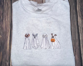 Puede incluir: Una sudadera gris con un diseño bordado de cuatro perros disfrazados de fantasmas para Halloween. Tres de los perros llevan disfraces de fantasmas tradicionales, mientras que el cuarto perro lleva una calabaza de Halloween.