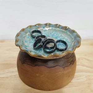 May include: A wooden bowl with a blue and brown glazed ceramic dish on top. The dish holds several black rings.