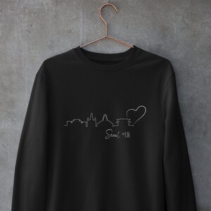 May include: Black sweatshirt with a white outline of the Seoul skyline and a heart, with the text "Seoul 서울" underneath.