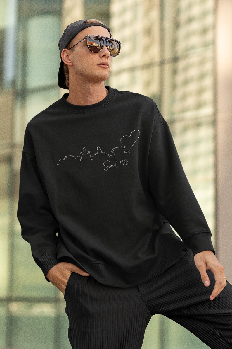 May include: Black sweatshirt with a white outline of the Seoul skyline and a heart. The text "Seoul 서울" is written below the skyline.