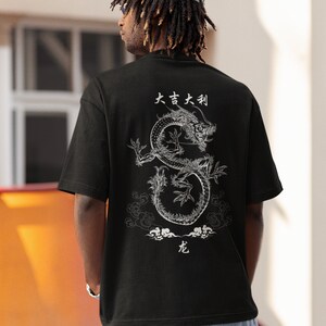 K&ouml;nnte beinhalten: Schwarzes T-Shirt mit einem wei&szlig;en Drachen-Motiv und japanischem Text, der "大吉大利" (ausgesprochen "Dai Kichi Dai Ritsu") lautet und "Gro&szlig;es Gl&uuml;ck, gro&szlig;er Wohlstand" bedeutet.