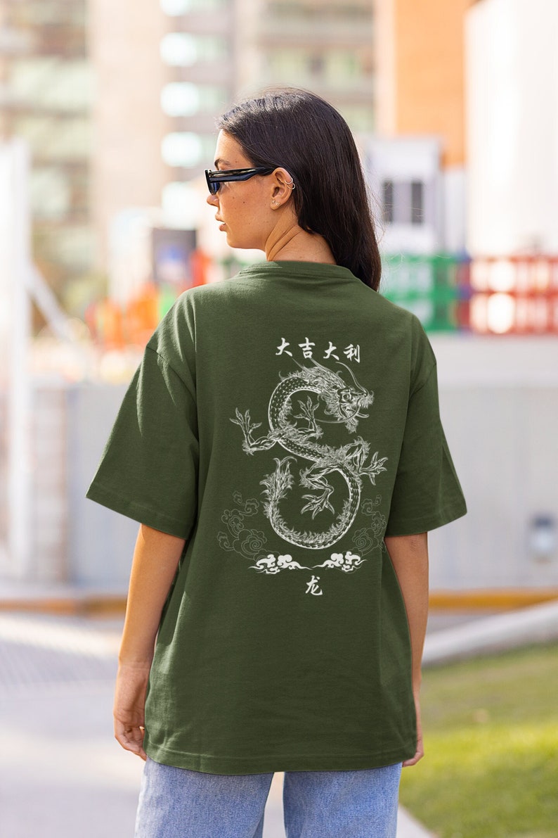 K&ouml;nnte beinhalten: Ein gr&uuml;nes T-Shirt mit einem wei&szlig;en Drachen-Motiv auf der R&uuml;ckseite. Der Drache ist von Wolken umgeben und dem Text "大吉大利" und "龙" in chinesischen Schriftzeichen.