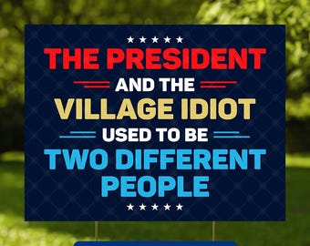May include: A dark blue yard sign with the text "THE PRESIDENT AND THE VILLAGE IDIOT USED TO BE TWO DIFFERENT PEOPLE." The sign has a red and gold color scheme with white stars and a blue rectangle at the bottom that says "SIGN & H-STAKE."