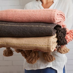 May include: A stack of three woven blankets with tassels. The blankets are pink, brown, and beige with gold accents.