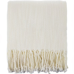 May include: A white throw blanket with a fringe border. The blanket is made of a soft, textured fabric.